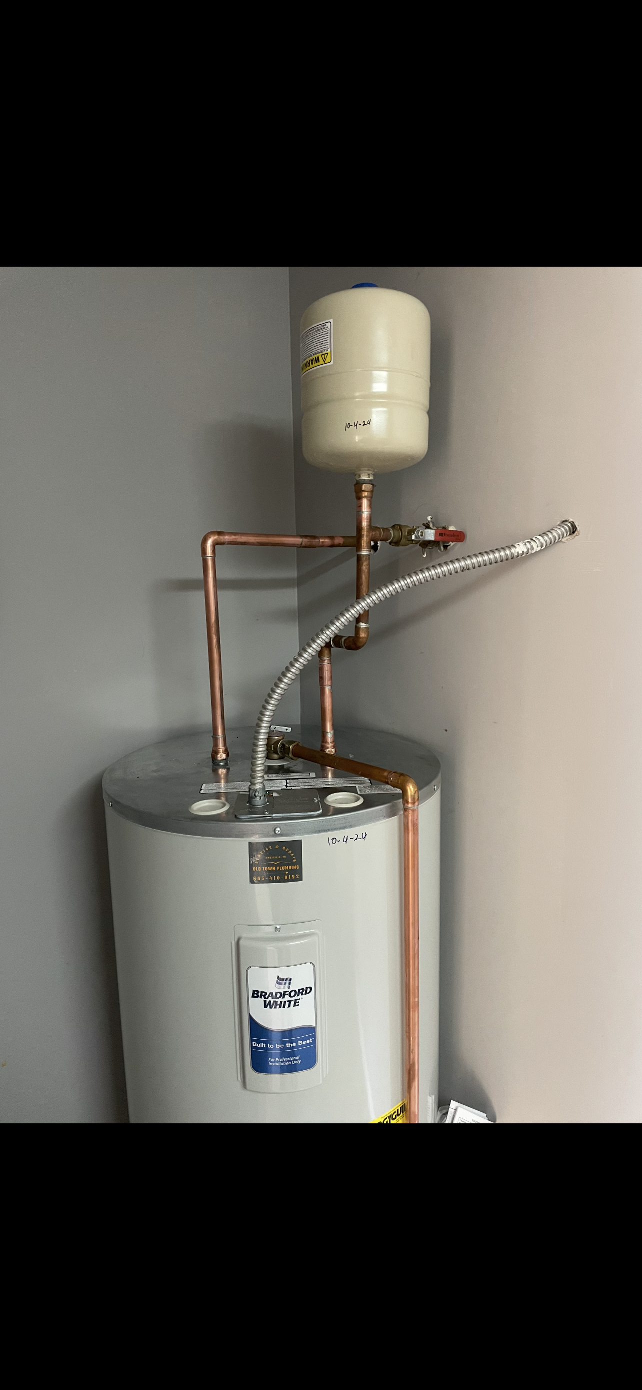 A water heater with copper pipes and an expansion tank installed in a corner of a room.