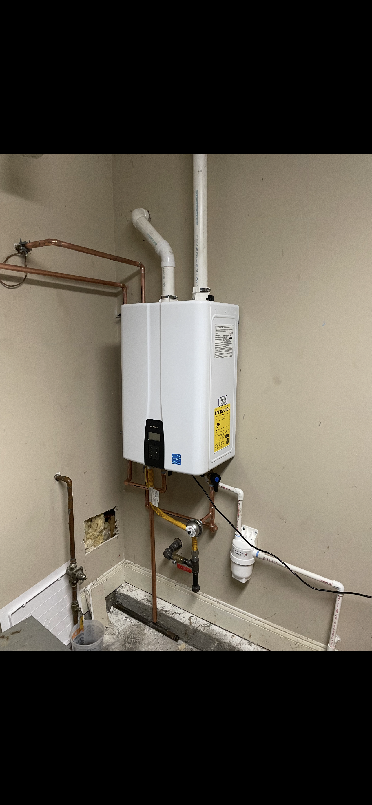 A tankless water heater installed in a basement corner, with copper pipes and exhaust vent.