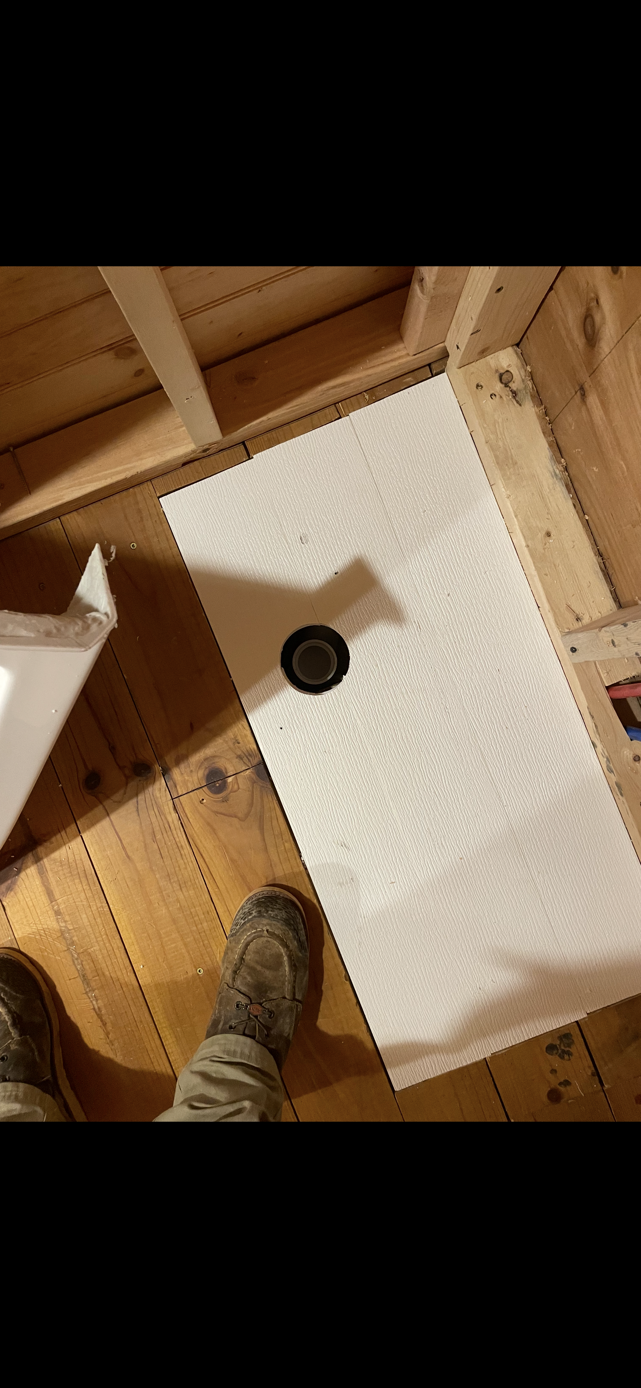 Shower pan with drain installed, in a wood-framed bathroom, surrounded by wood. A person is standing.