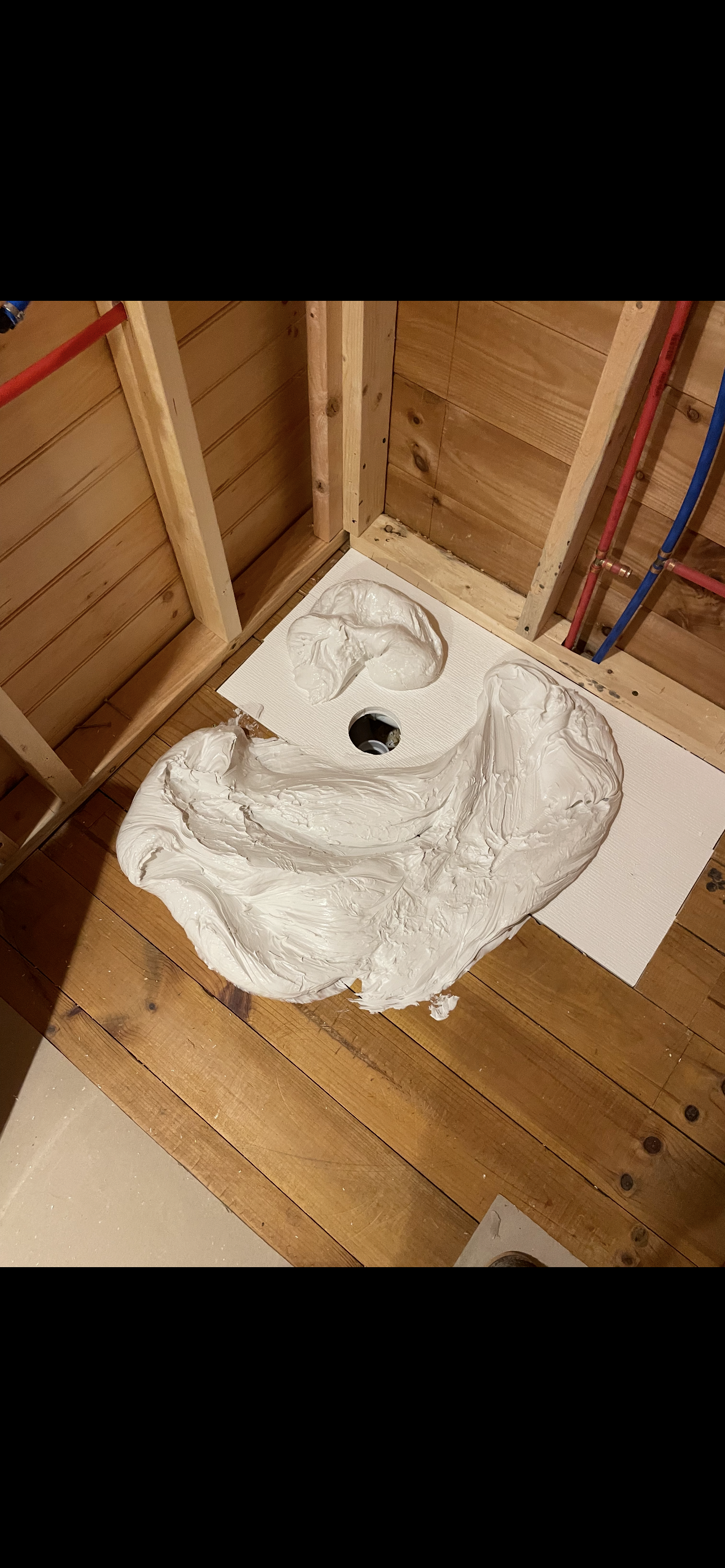 Shower floor with a mortar base, framed by wood studs and pipes.