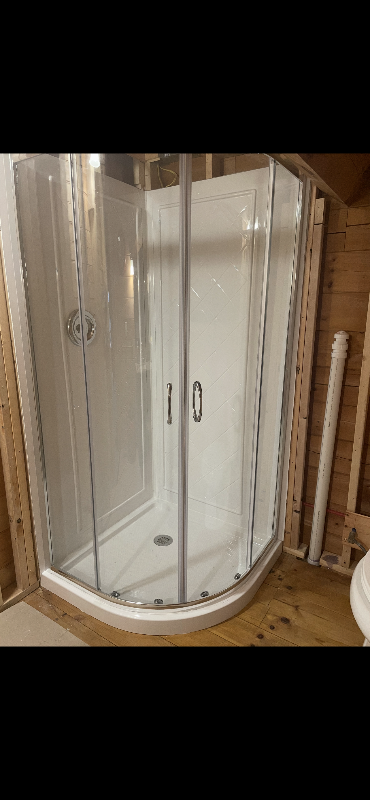 A corner shower stall is installed in a bathroom under construction.