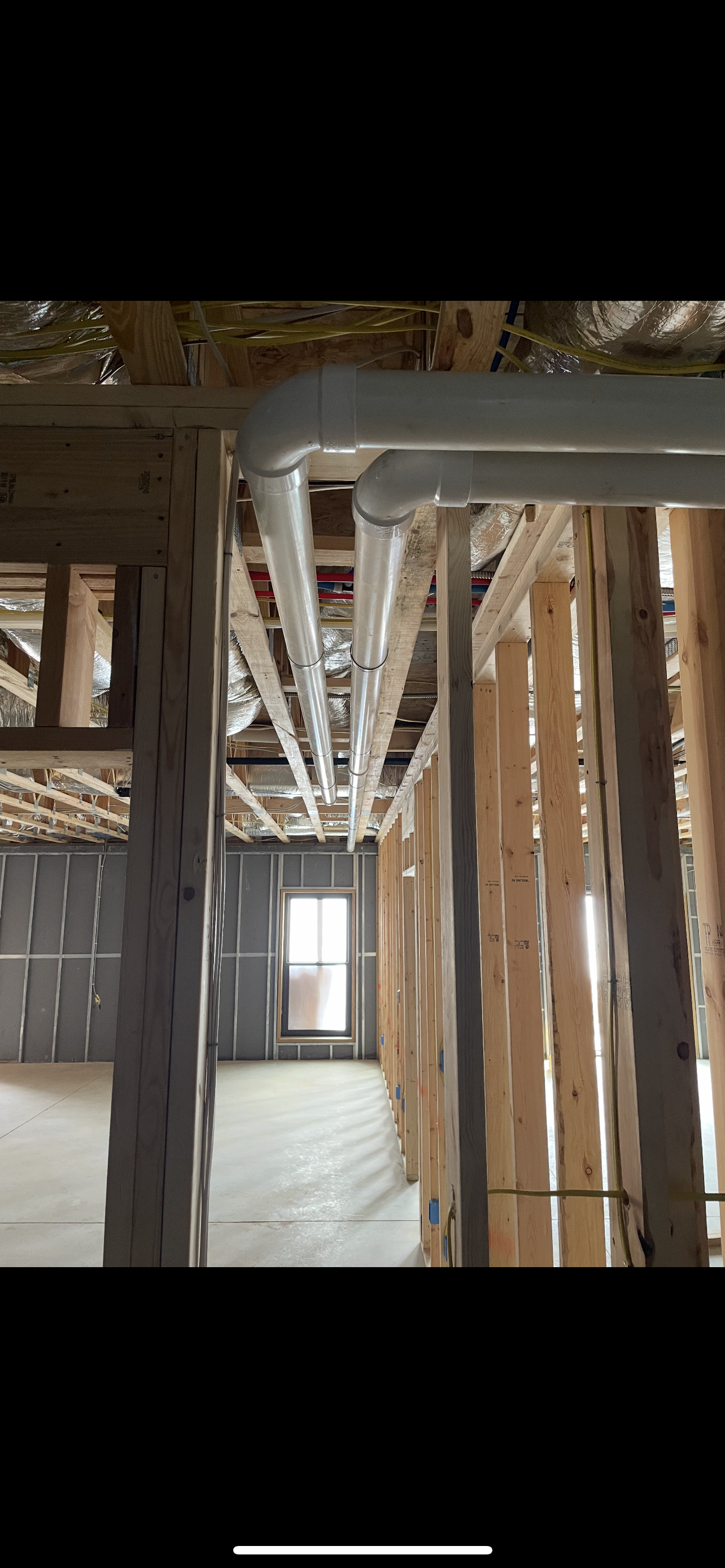 Interior view of a construction site, showing exposed beams, piping, and a doorway at the end of a hallway.