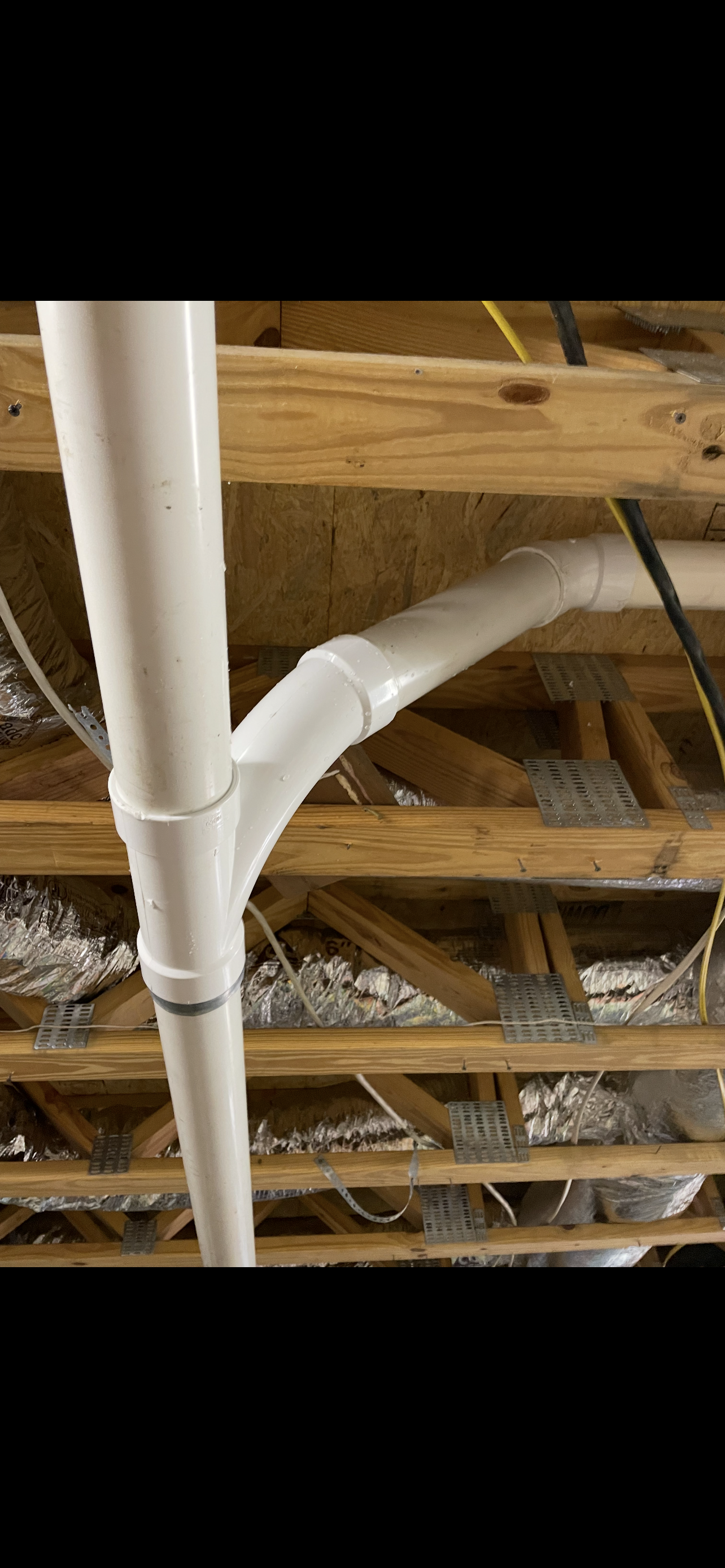 White PVC plumbing pipes connected in a Y-shape under a wooden ceiling.