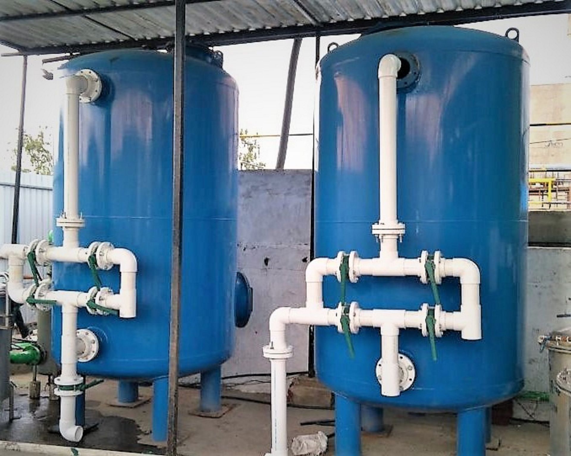 Two tall blue water filtration tanks with white piping in an outdoor setting.