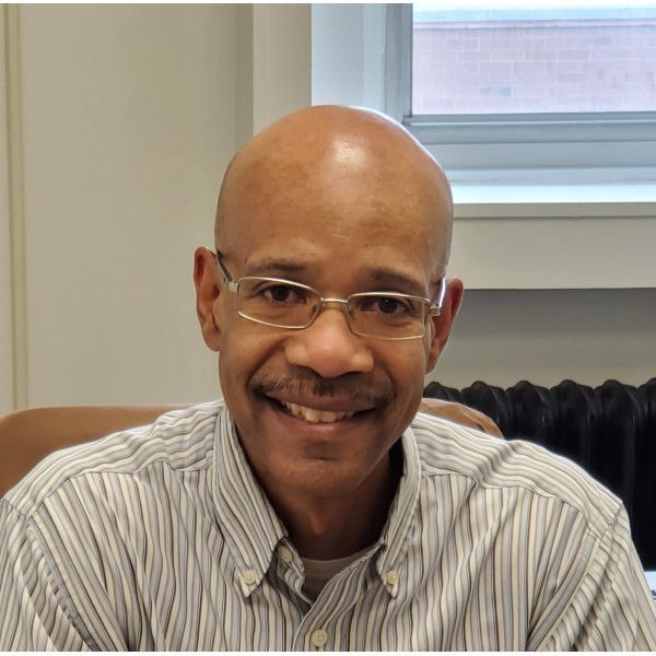 A bald man wearing glasses and a striped shirt smiles for the camera