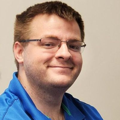A man wearing glasses and a blue shirt is smiling for the camera