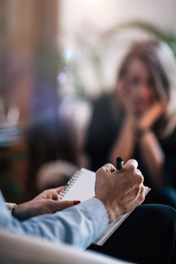 A woman is sitting in a chair while a man writes in a notebook