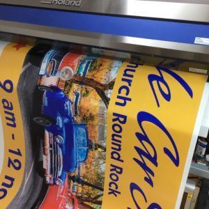 A large format printer printing a yellow sign with a blue car graphic and text: 