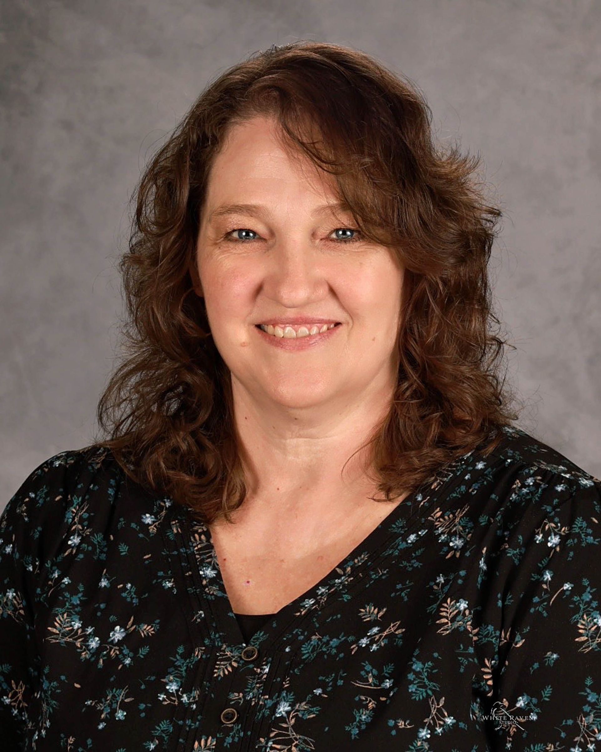 A woman in a floral shirt and a black jacket is smiling for the camera.