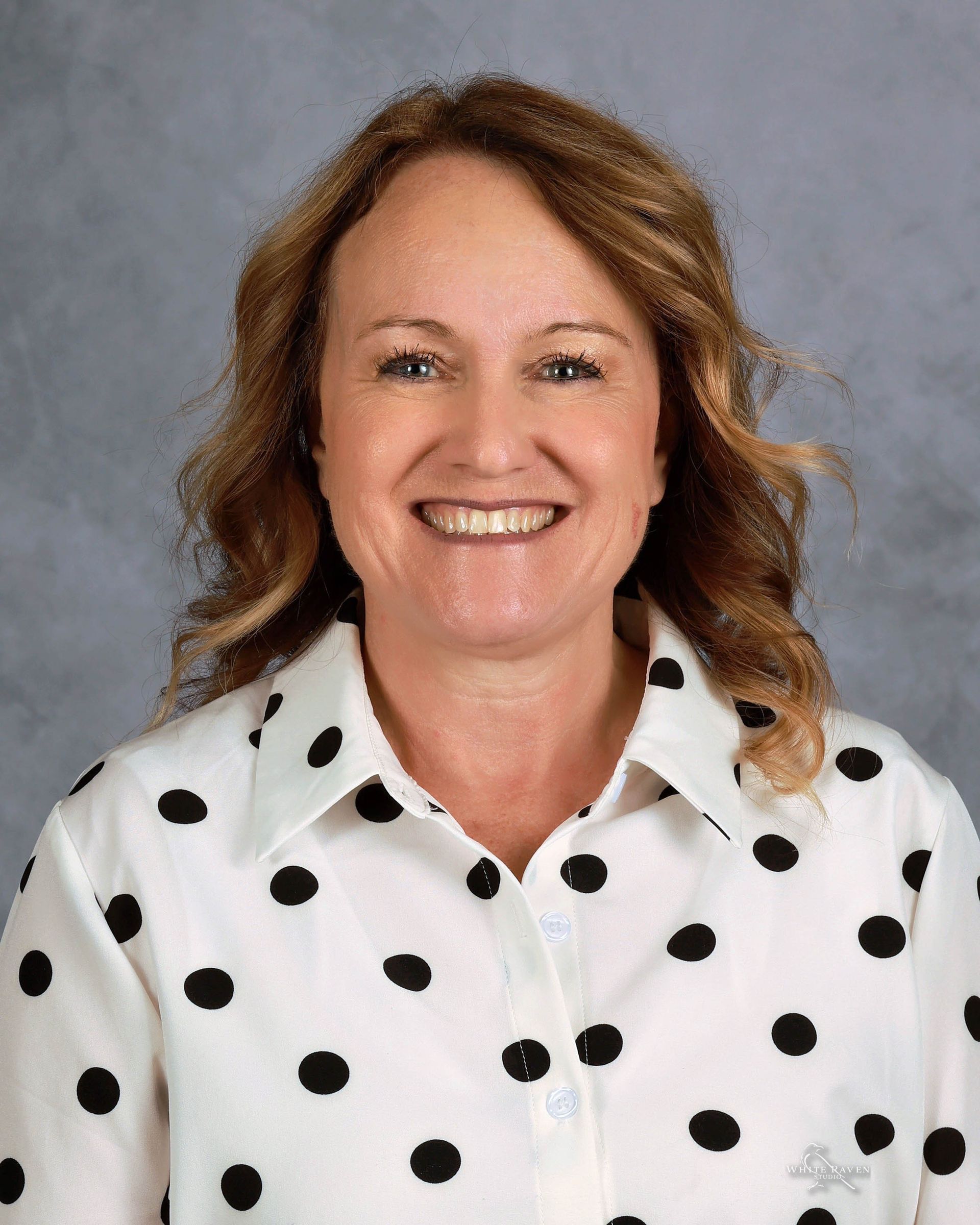 A woman in a white shirt with flowers on it is smiling for the camera.