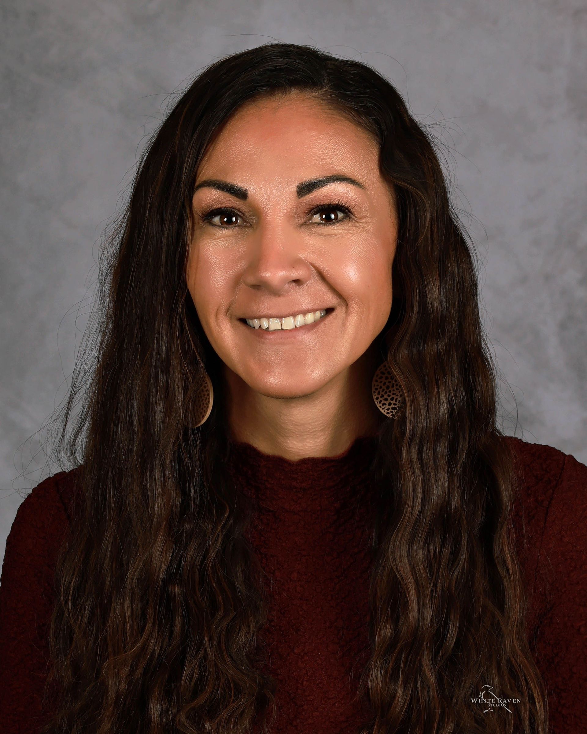 A woman with long hair and red earrings is smiling for a picture.