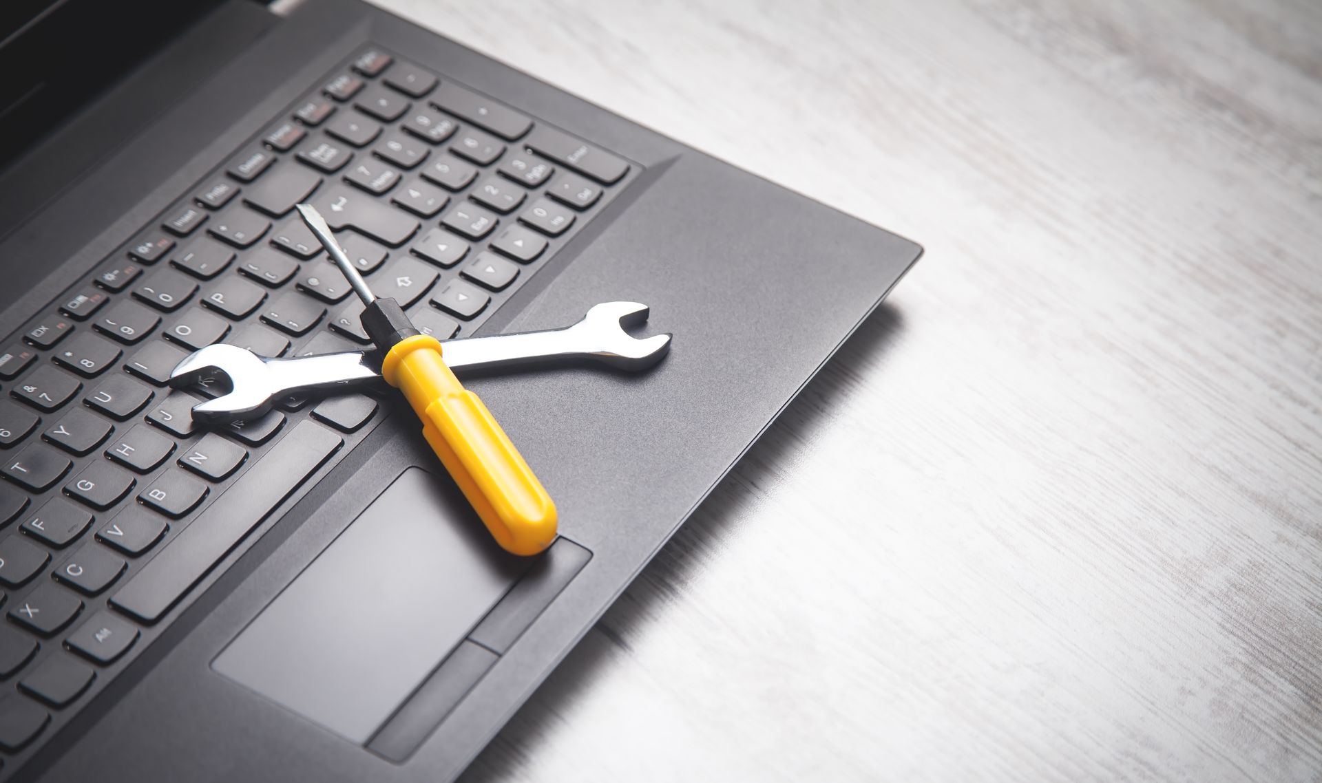 A laptop with a wrench and screwdriver on the keyboard