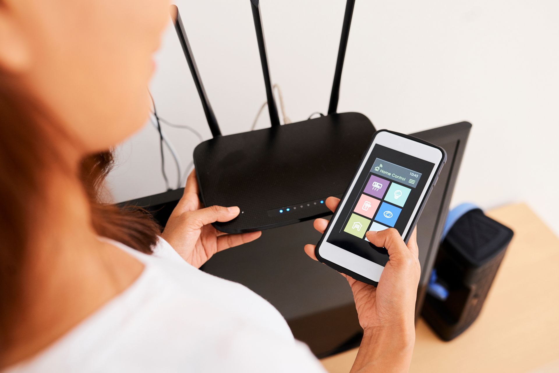 A woman is holding a cell phone in front of a router.