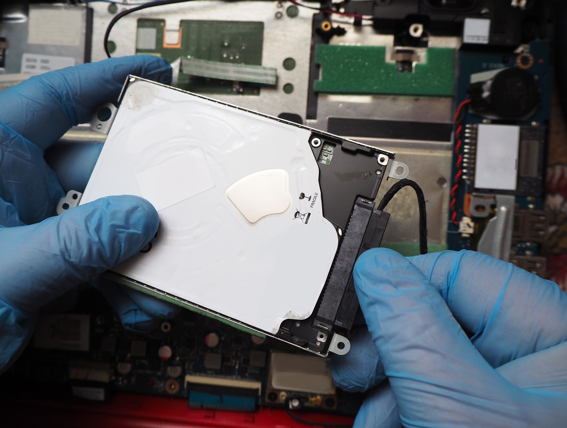 A person wearing blue gloves is holding a hard drive in their hands.