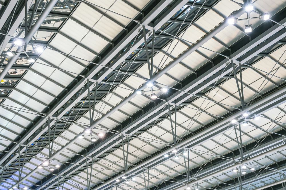 Techo industrial con cerchas de acero, tragaluces y luces cenitales brillantes.