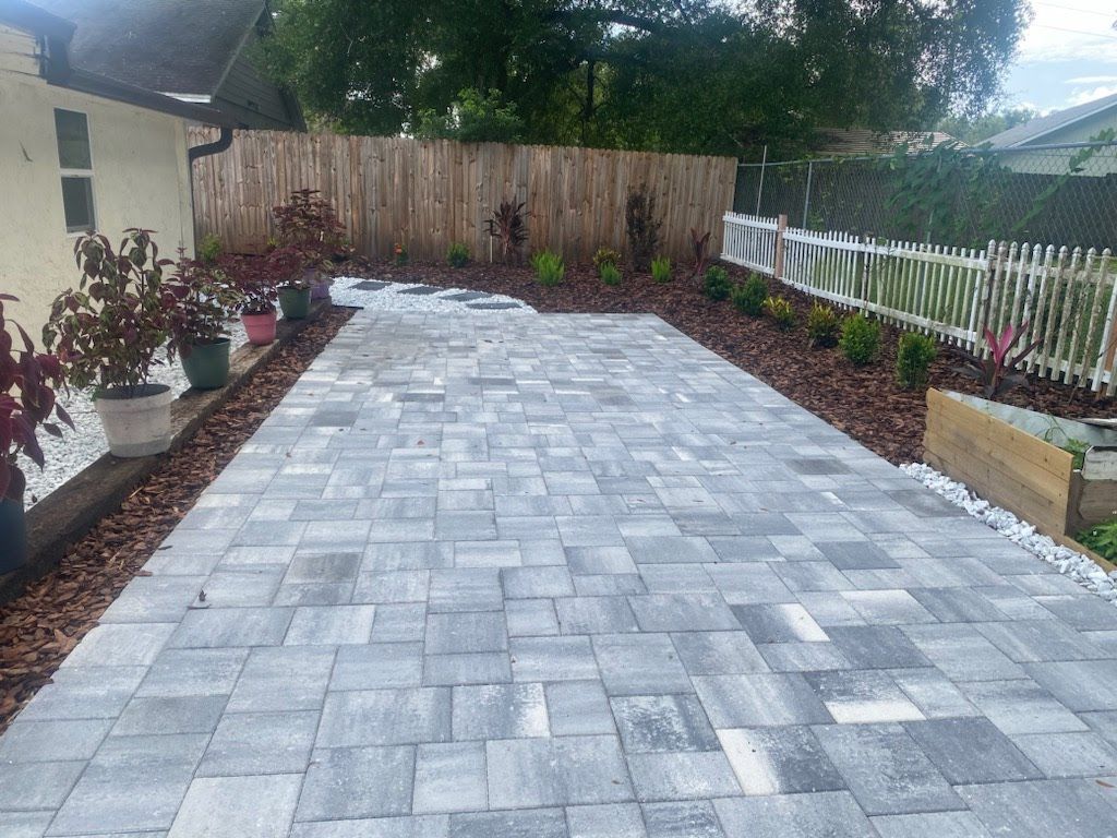 A brick driveway leading to a wooden fence in a backyard.