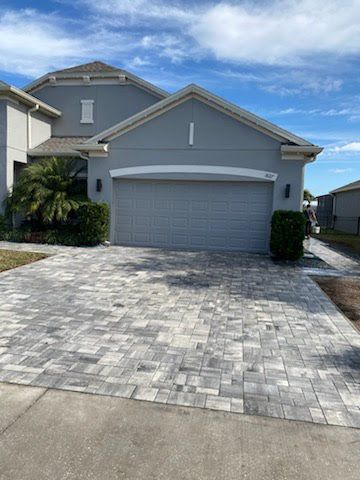 A large gray house with a brick driveway in front of it.