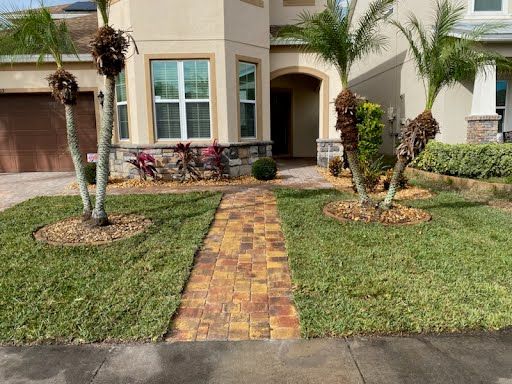 A house with a brick walkway leading to it and palm trees in front of it.