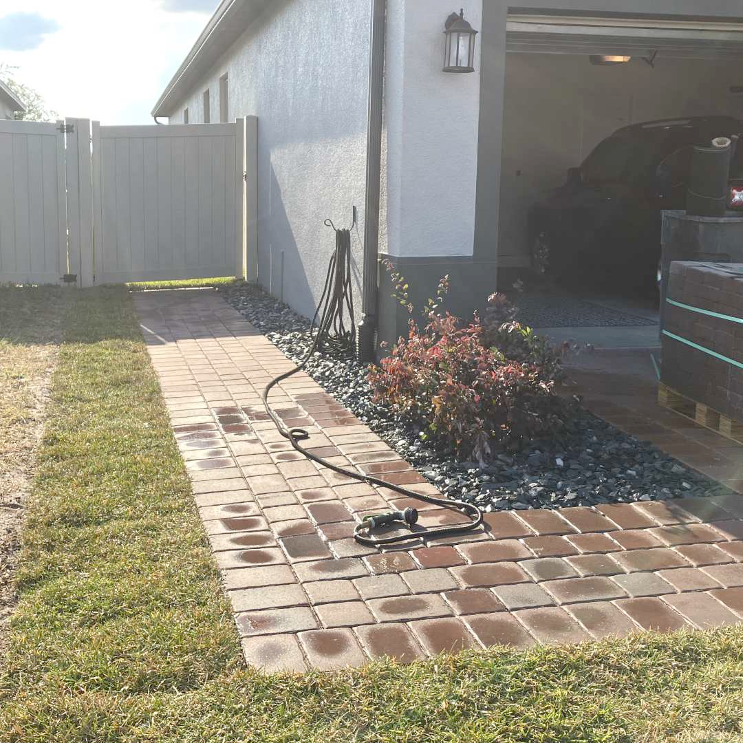 A brick walkway leading to a garage with a car parked in it.