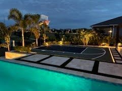 Backyard with lit swimming pool and basketball half-court at dusk