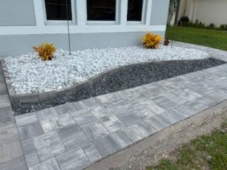 Modern front walkway with gray pavers, stone border, and white gravel landscaping by a house