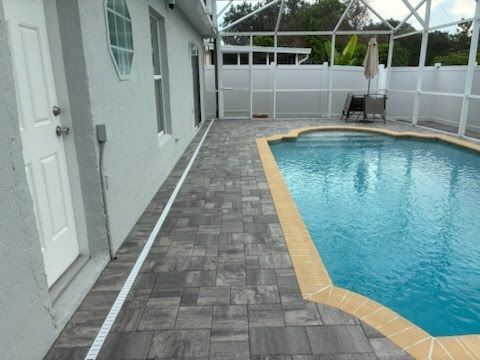 Patio beside a swimming pool with gray pavers and a screened enclosure