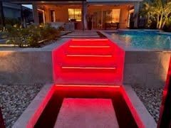 Red-lit outdoor steps leading to a modern house entrance beside a pool at night