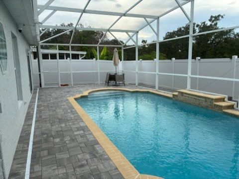 Covered backyard pool with blue water, gray paver deck, white screen enclosure, and stepped spa ledge