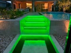 Bright green-lit steps descend to a pool at a modern patio at night