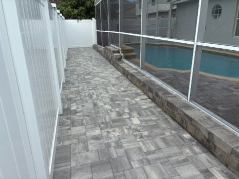 Narrow stone walkway beside a white fence and screened pool enclosure, with a blue pool on the right.