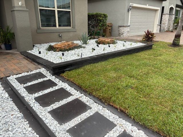 Front yard with dark stepping stones, white gravel beds, and green lawn beside a house and garage.