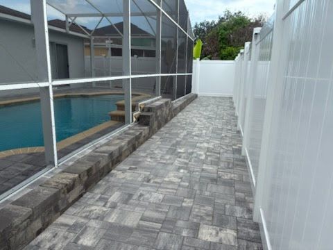 Paved poolside walkway beside a screened-in pool and white fence in a backyard