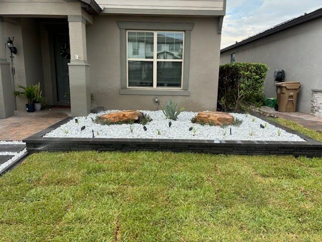 Front yard with a green lawn, white gravel bed, and small shrubs in front of a house.