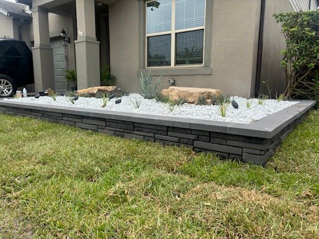 Raised front yard planter with gray stone edging, white gravel, succulents, and boulders beside a house