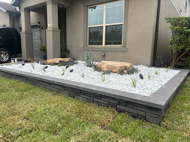 Front yard xeriscape with white gravel, rocks, and sparse plants beside a house and window