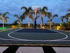 Outdoor basketball court at dusk with palm trees and a hoop under a cloudy sky