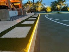 Modern backyard patio at dusk with illuminated stepping stones, pool deck, and palm trees