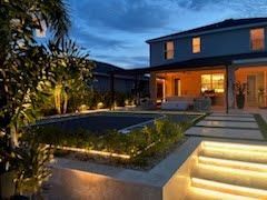 Modern house with a lit pool and landscaped backyard at dusk