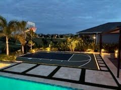Outdoor sports court with lights, surrounded by palm trees at dusk.
