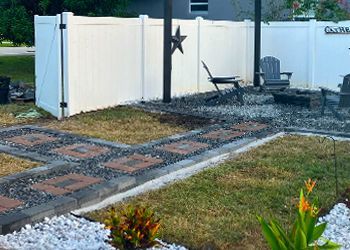 A white fence surrounds a yard with a walkway and chairs.