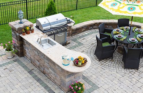 A patio with a grill , sink , table and chairs.