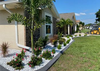 A house with a garden in front of it and a yellow tractor in the background.