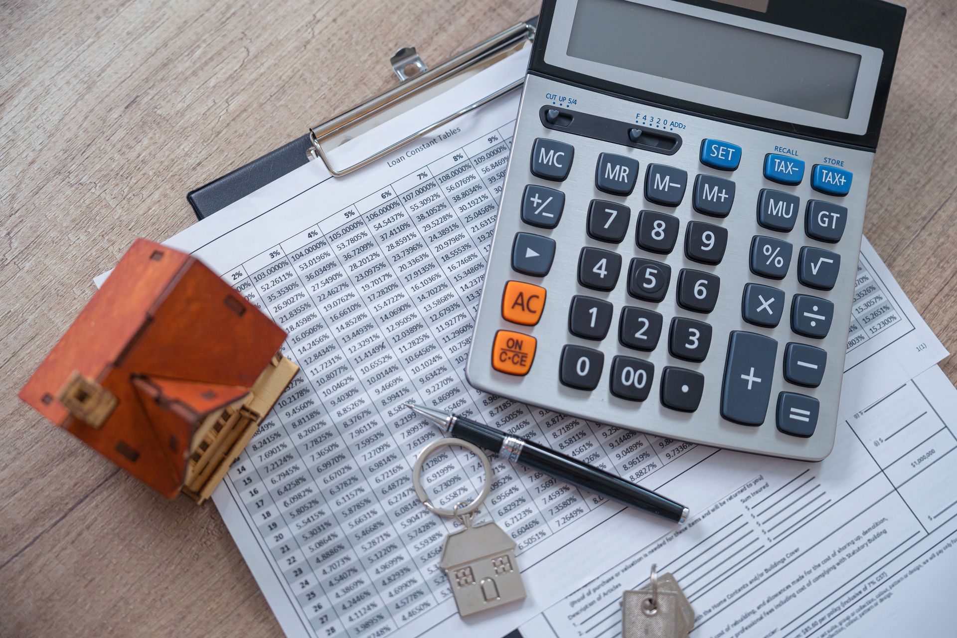 A calculator , keys , a pen , and a model house are on a clipboard.