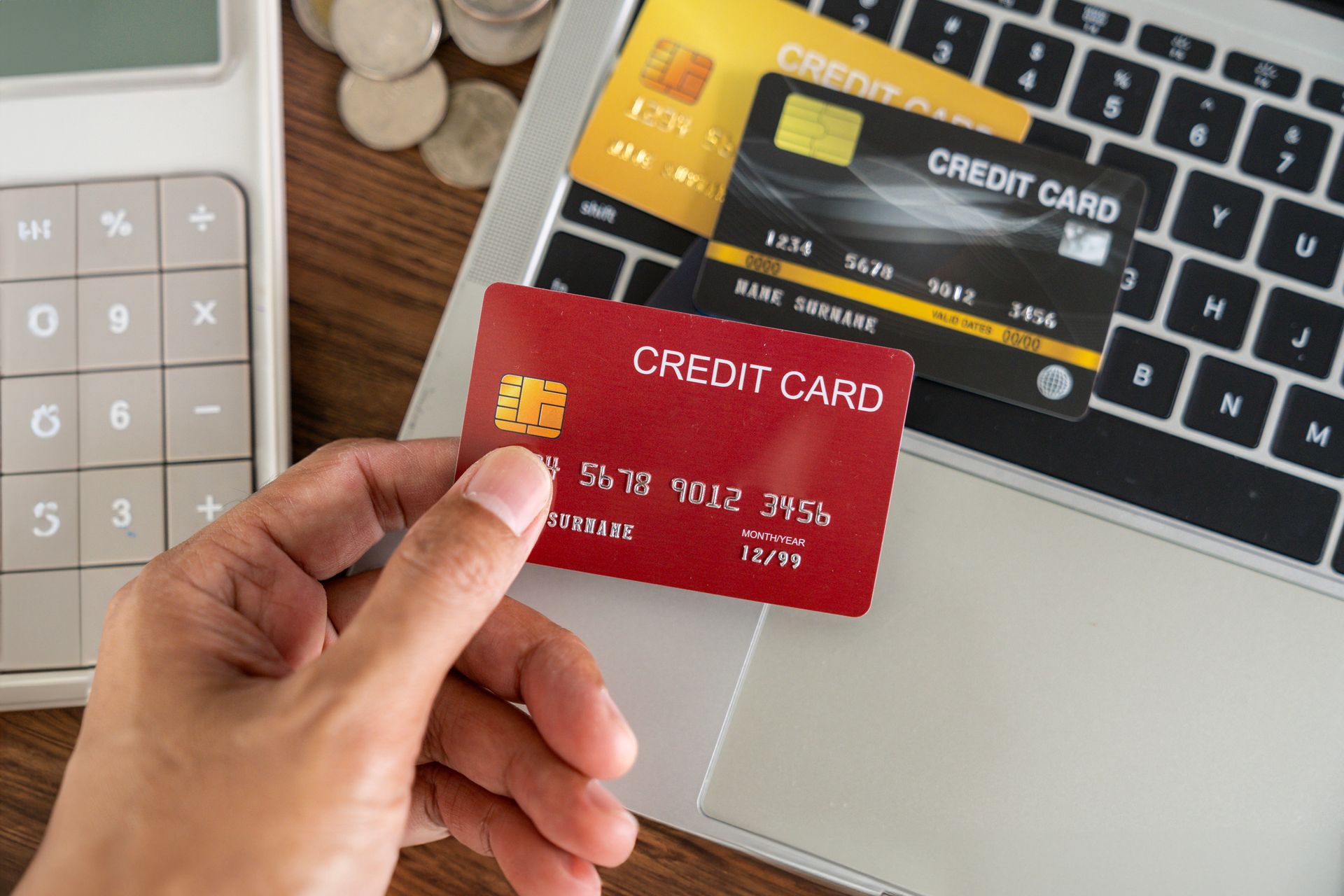 A person is holding a credit card in front of a laptop.