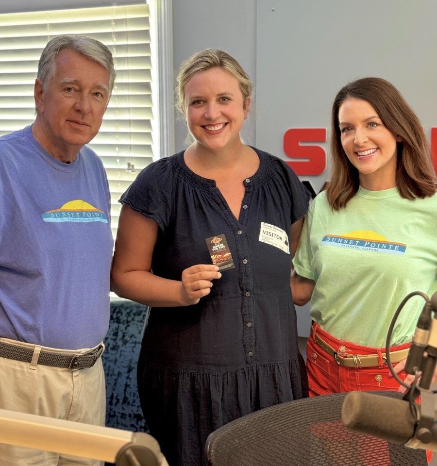 Three people smiling at a table, holding a small item indoors.