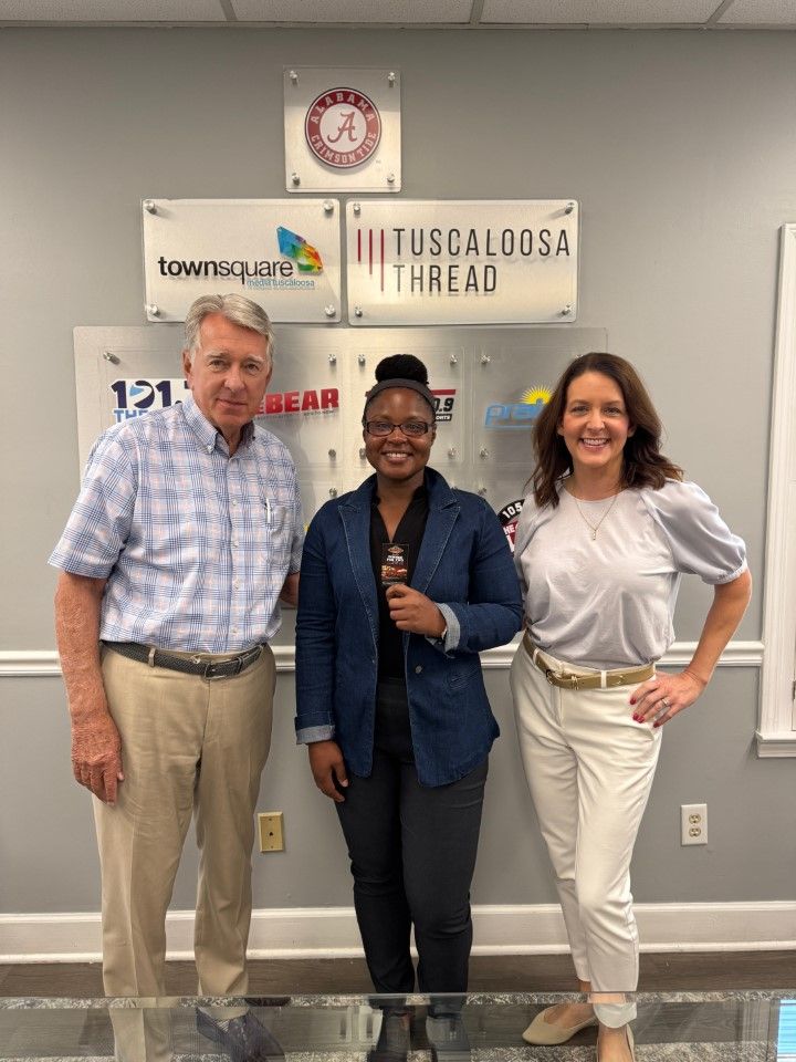 Three people smiling and standing in front of a wall with business signs.