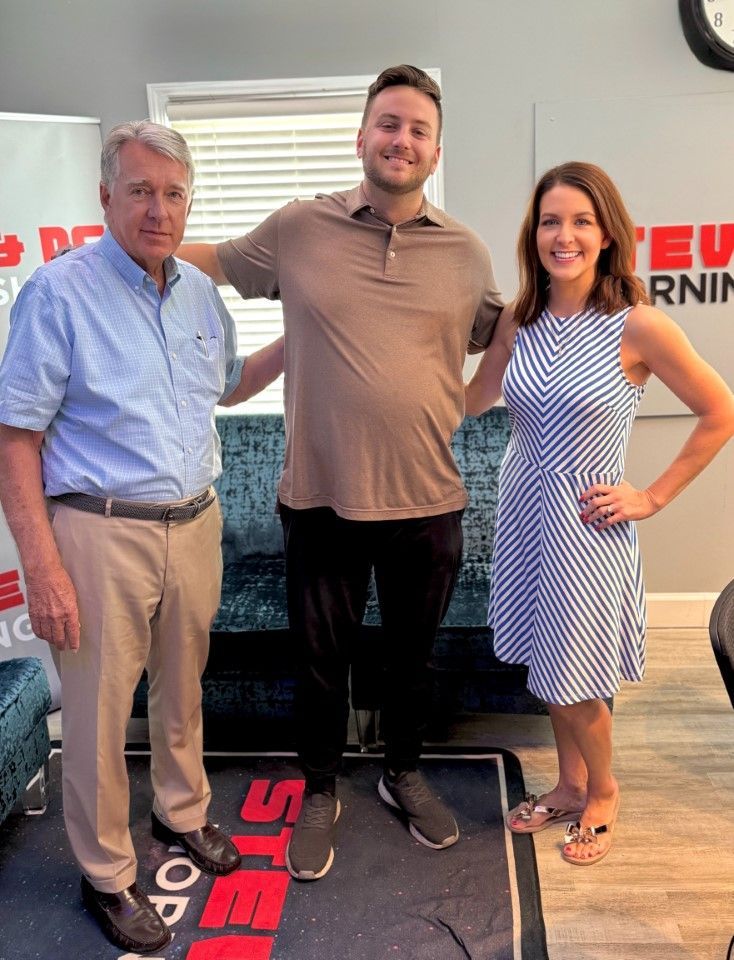 Three people standing indoors at a promotional event, smiling in front of a branded backdrop.
