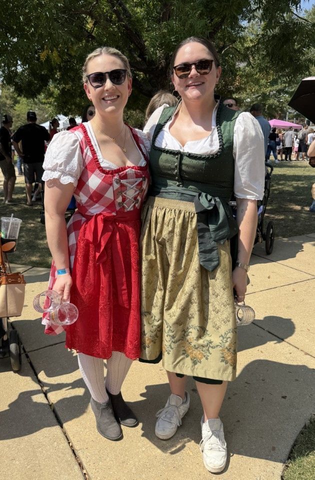 Two people in festive dresses and sunglasses standing together outdoors on a sunny day.