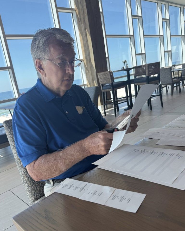 Man in a blue shirt reading papers at a table in a bright waterfront restaurant