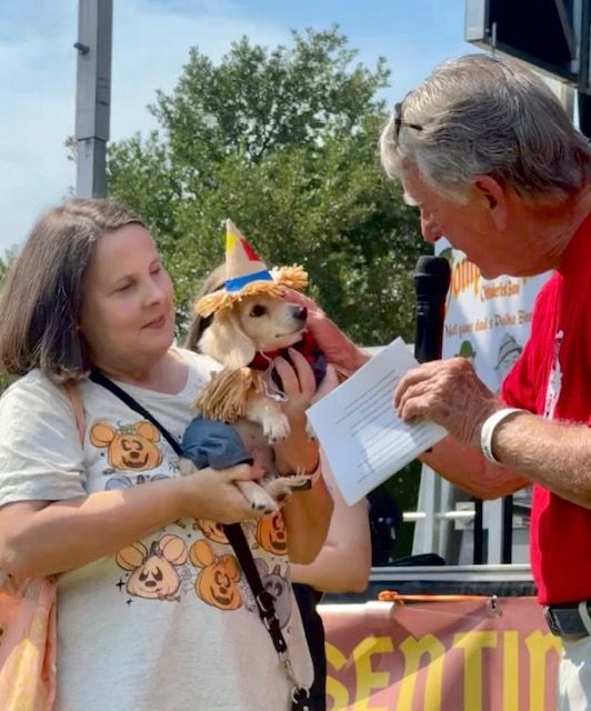Woman holding a small dog in a party hat while a man in red writes on a form outdoors